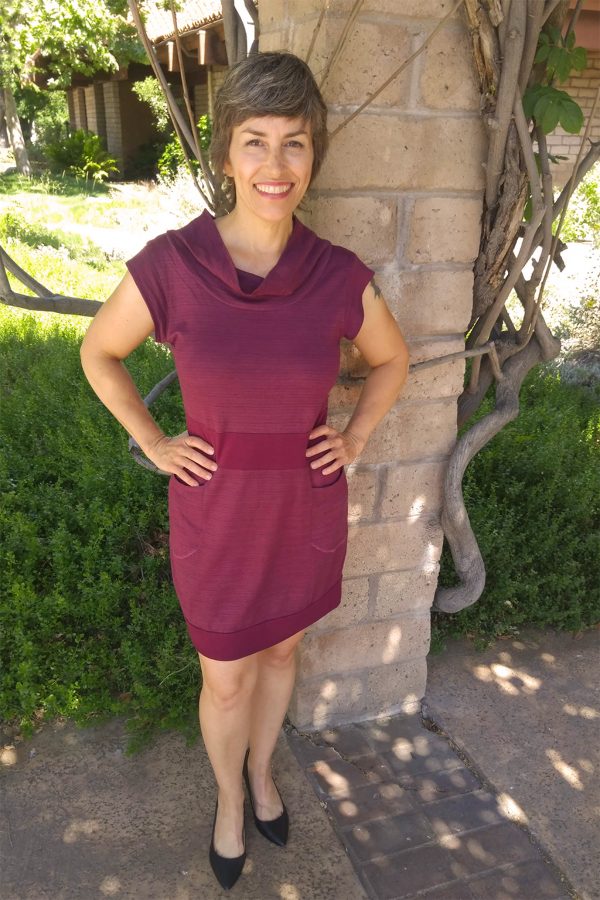 short sleeve dress with cowl neck and pockets on lady in front of a column of bricks and tree branches