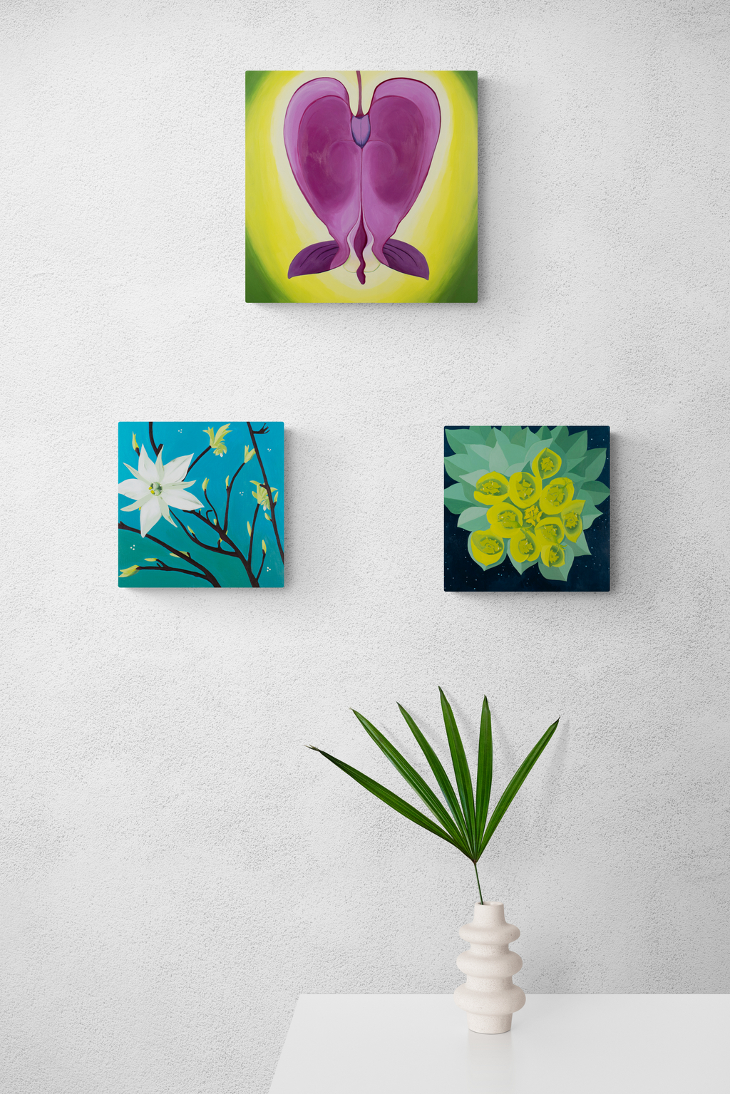 three flower paintings by Amy Daileda on wall with palm frond in vase